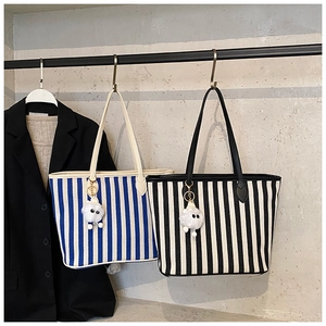 Close-up of striped canvas tote bag with playful pom-pom charm and durable PU handles