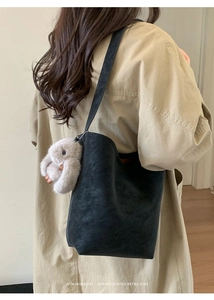 Minimalist black bucket bag with soft plush rabbit charm shown on model shoulder