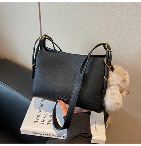 Close-up of black pebble leather handbag featuring a plush rabbit charm and gold hardware