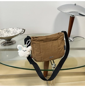 Détail d'un sac seau en nylon marron avec bandoulière noire et breloque lapin en peluche blanc