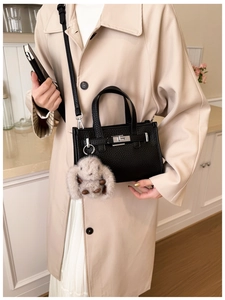 Close-up of black lychee grain leather handbag with silver lock and plush rabbit charm