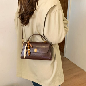 Détail du sac bandoulière vintage marron foncé avec pompon en bois et boucle dorée