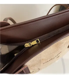 Close-up of smooth gold zipper and beige suede with brown leather stitching on a tote