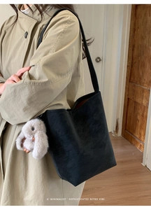 Minimalist black bucket bag with plush rabbit charm shown on model in warm indoor setting