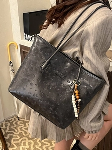 Black leather tote bag with embossed pattern and beaded charm shown by model indoors