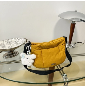 Gros plan du sac bandoulière matelassé jaune gingembre avec pendentif sur table en verre