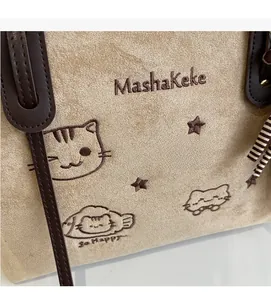 Detail of beige suede tote bag featuring cat embroidery and dark brown leather strap