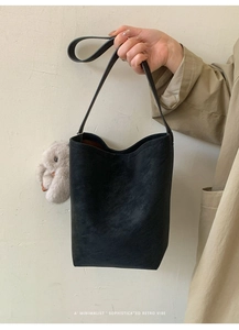 Close-up of black matte bucket bag with a cute plush bunny charm and shoulder strap