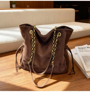 Détail de sac cabas en daim marron foncé avec chaîne dorée et cordon de serrage précis