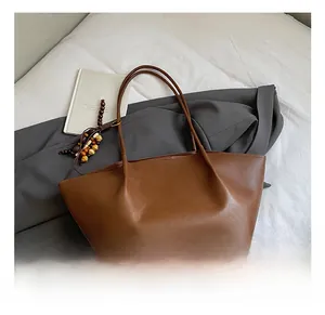 Brown leather tote bag with stylish wooden bead charm and slim straps on white bedding