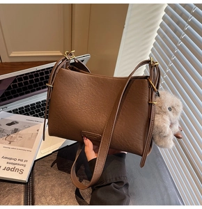 Detailed shot of brown pebbled leather bag with plush rabbit charm and gold hardware