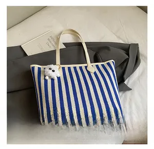 Detail view of blue and white striped canvas tote bag with white plush ball charm accessory