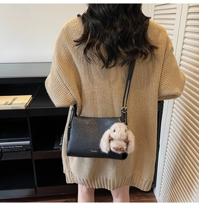 Detail of black textured leather bag with cute grey plush rabbit charm and slim shoulder strap