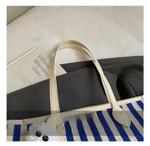 Detail of blue and white striped woven tote bag with cream leather handle and plush charm