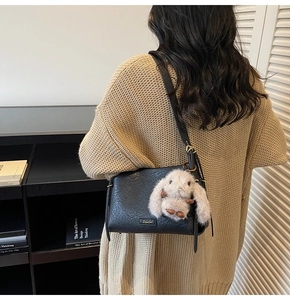 Detail of black pebbled leather crossbody bag with cute plush bunny charm and golden buckle