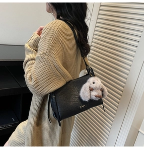 Detail of black textured leather shoulder bag with a cute long-eared plush rabbit charm