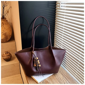 Detail view of deep wine red leather tote bag with wooden bead charm in a retro setting