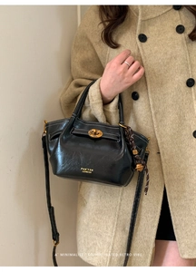 Detailed view of black leather bucket bag with white stitching and gold planet clasp