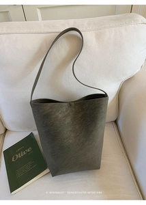 Detail of dark grey-green bucket bag with lychee texture on a minimalist white sofa