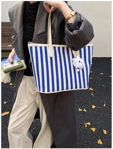 Detail of blue striped canvas tote bag with white faux fur pompom and leather handle