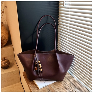 Detail of vintage burgundy leather tote bag with wooden bead charm on a wooden surface