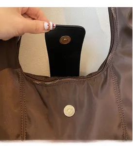 Detail of golden magnetic snap closure and fine stitching on a brown nylon shoulder bag