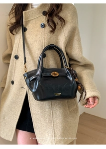 Detail of retro black leather bucket bag featuring gold clasp and brand logo