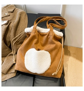 Detail of plush tote bag with white apple applique and drawstring closure on a suede surface