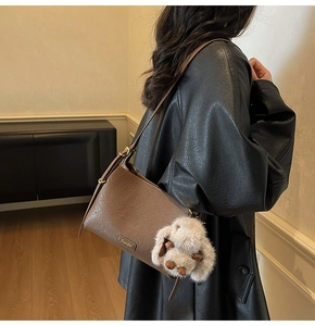 Detail of brown leather shoulder bag with plush rabbit charm and gold buckle