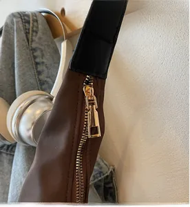 Detail of smooth gold-tone metal zipper and leather strap on brown nylon crescent bag