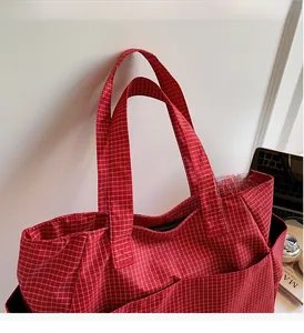Detail of red and white checkered canvas tote bag with reinforced handles and front pocket