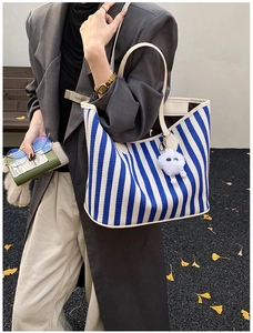 Close-up of blue striped canvas tote bag with white leather straps and plush charm