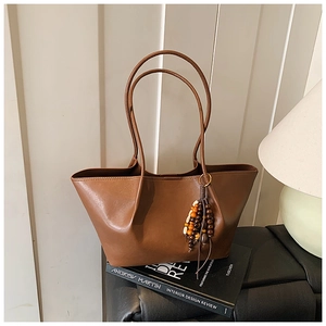 Detailed macro view of the brown leather tote bag with unique wooden beaded tassel accessory