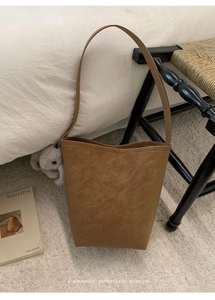 Brown vintage bucket bag with a white bunny charm on a beige woven rug background