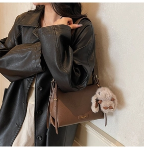 Detail of dark brown leather crescent bag with gold logo and plush rabbit charm