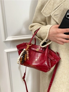 Elegante borsa rossa con motivo a coccodrillo, finiture dorate e ciondolo a perle