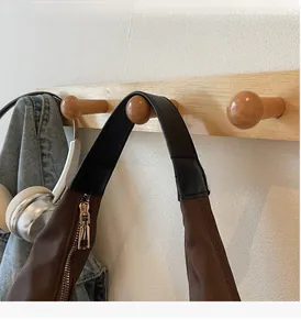 Brown nylon hobo bag featuring black leather handle and gold zipper on a wooden hook