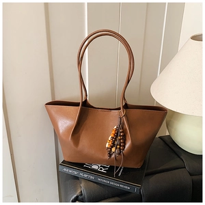 Detail of caramel brown tote bag with colorful beaded tassel on minimalist background
