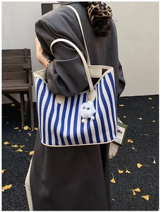 Detail of blue striped canvas tote bag with cream leather trim and plush charm