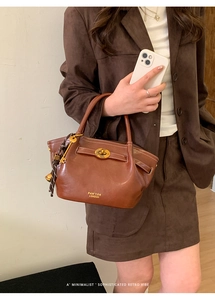 Detail of a dark brown leather handbag with a gold-tone turn-lock and key pendant