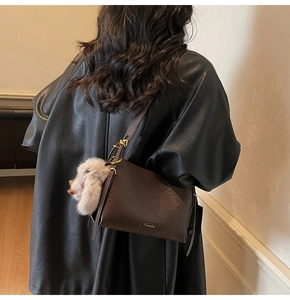 Detail of a dark brown leather baguette bag with metal logo and plush bunny charm