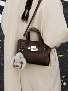Dark brown leather tote bag with silver buckle and plush rabbit charm on a beige coat