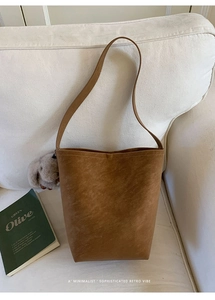 Brown leather bucket bag with plush bunny charm placed on a minimalist sofa with a book