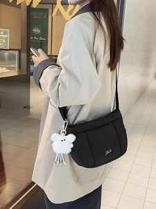 Sac seau noir matelassé avec charme en peluche porté sur un trench-coat beige élégant