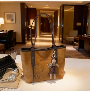 Brown suede tote bag with cartoon embroidery and a cute rabbit plush pendant in a cozy office