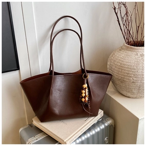 Detail of dark brown leather tote bag with wooden bead charm on a vintage suitcase