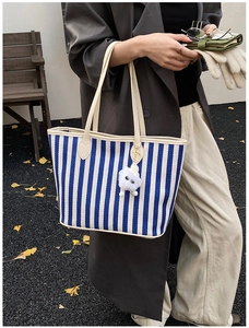 Detail of blue and white striped canvas tote with plush monster charm and leather straps