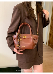 Detail of retro brown leather tote with gold oval lock and elegant bell pendant
