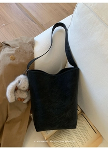 Detail of a black matte bucket bag with a cute plush bunny charm on a beige sofa