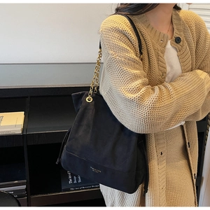 Détail macro du sac cabas en daim matelassé noir avec bandoulière en chaîne dorée chic